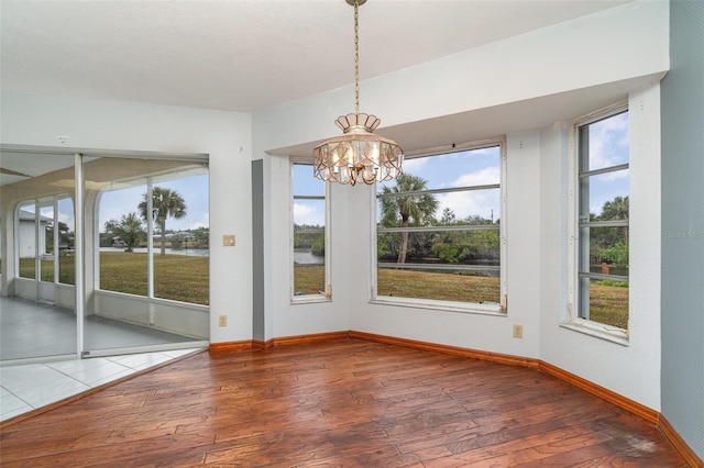 unfurnished dining area featuring wood-type flooring, a chandelier, plenty of natural light, and a water view