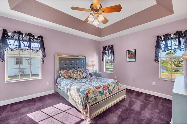 bedroom with dark colored carpet, ceiling fan, and a raised ceiling