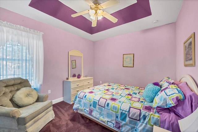 bedroom with a raised ceiling, ceiling fan, and dark carpet