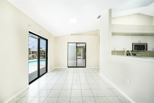 tiled empty room with plenty of natural light, lofted ceiling, and sink