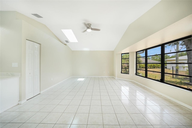 empty room with lofted ceiling with skylight, ceiling fan, and light tile patterned floors