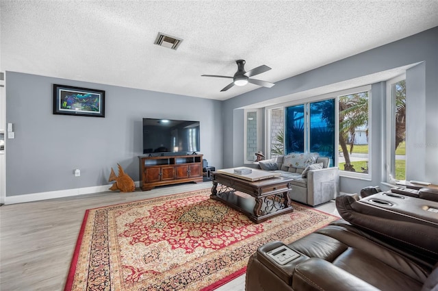 living room with ceiling fan, a textured ceiling, and light wood-type flooring