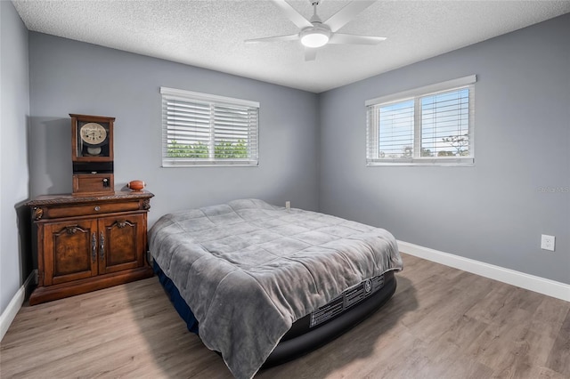 bedroom with ceiling fan, light hardwood / wood-style floors, a textured ceiling, and multiple windows