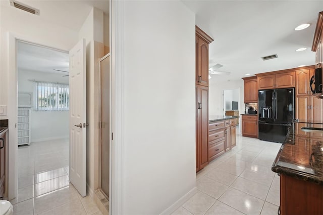 kitchen with black refrigerator with ice dispenser, ceiling fan, dark stone counters, and light tile patterned flooring