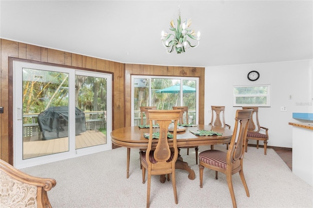 carpeted dining space with a chandelier and wood walls