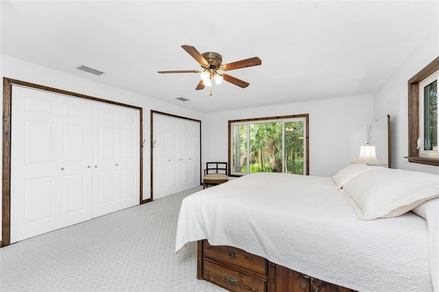 bedroom with ceiling fan, light colored carpet, and two closets