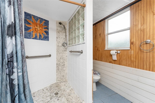 bathroom featuring tiled shower, wood walls, tile patterned floors, and toilet