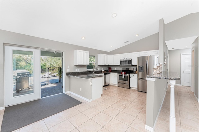 kitchen with white cabinets, kitchen peninsula, lofted ceiling, light tile patterned floors, and appliances with stainless steel finishes