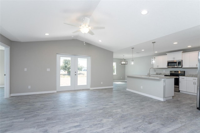 kitchen featuring appliances with stainless steel finishes, a kitchen island with sink, white cabinetry, hanging light fixtures, and lofted ceiling