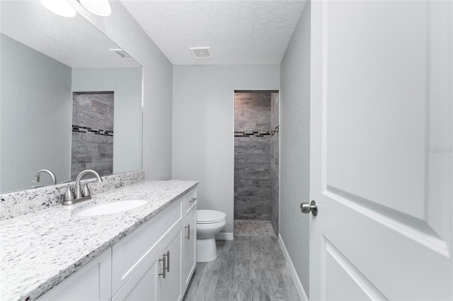 bathroom featuring vanity, hardwood / wood-style flooring, toilet, tiled shower, and a textured ceiling