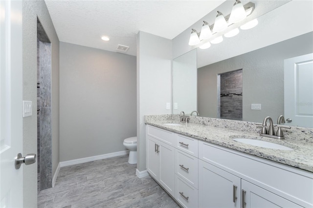 bathroom with a textured ceiling, vanity, toilet, and walk in shower