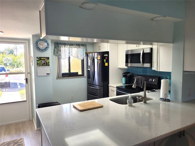 kitchen with white cabinets, light wood-type flooring, appliances with stainless steel finishes, tasteful backsplash, and kitchen peninsula