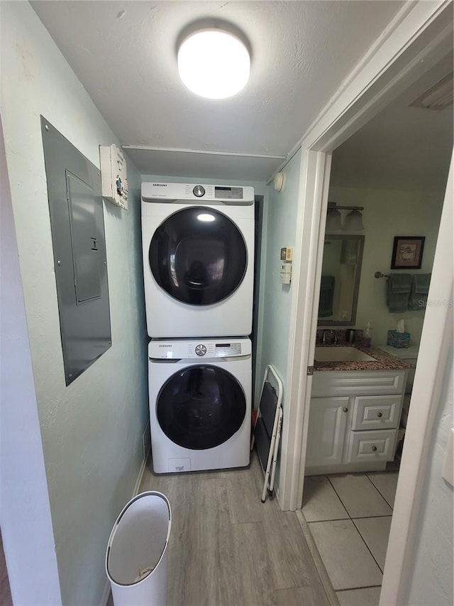 laundry room with stacked washing maching and dryer, sink, electric panel, and light hardwood / wood-style flooring