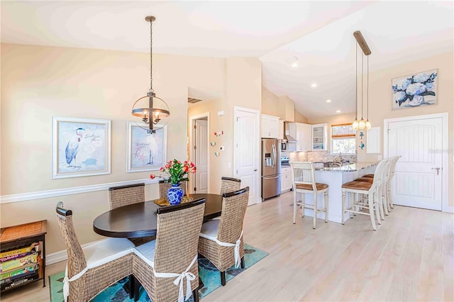 dining area with light wood-type flooring, high vaulted ceiling, and a chandelier