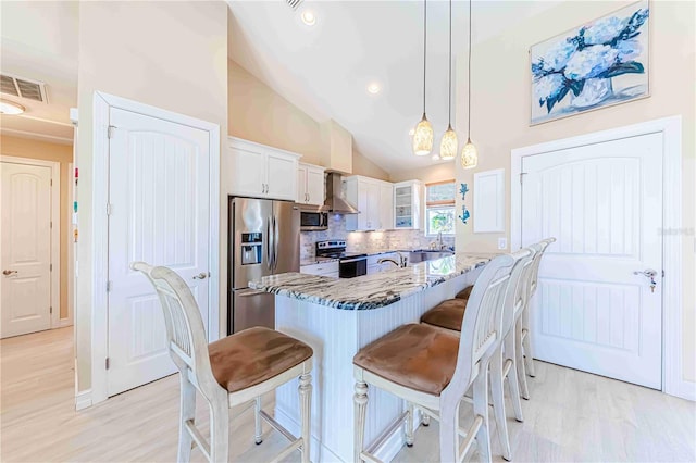 kitchen featuring light stone counters, white cabinetry, decorative light fixtures, wall chimney range hood, and stainless steel appliances