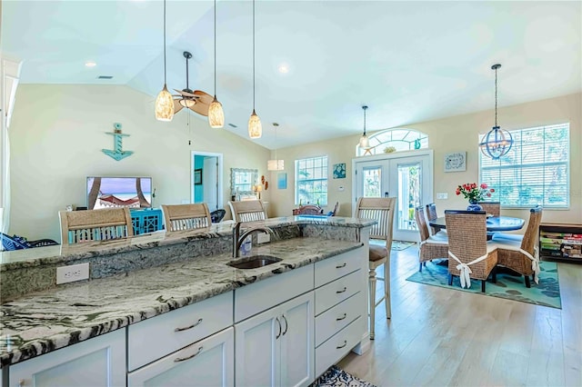 kitchen featuring hanging light fixtures, light stone countertops, sink, white cabinetry, and a kitchen bar