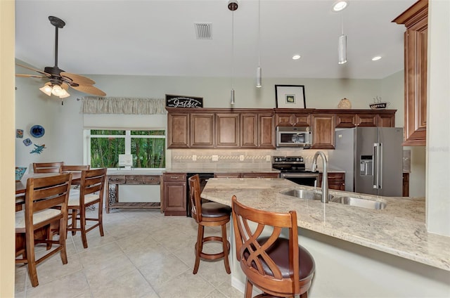 kitchen with light stone countertops, sink, hanging light fixtures, and appliances with stainless steel finishes