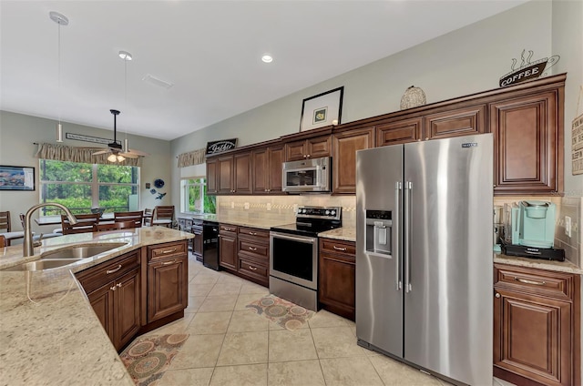 kitchen featuring sink, hanging light fixtures, tasteful backsplash, light stone counters, and appliances with stainless steel finishes