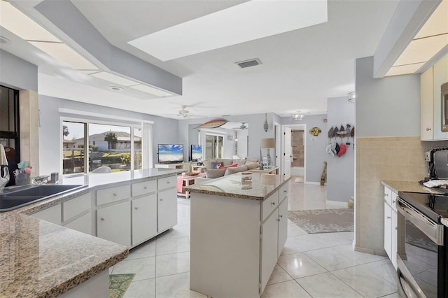 kitchen featuring white cabinets, ceiling fan, stainless steel electric range oven, light tile patterned floors, and a kitchen island