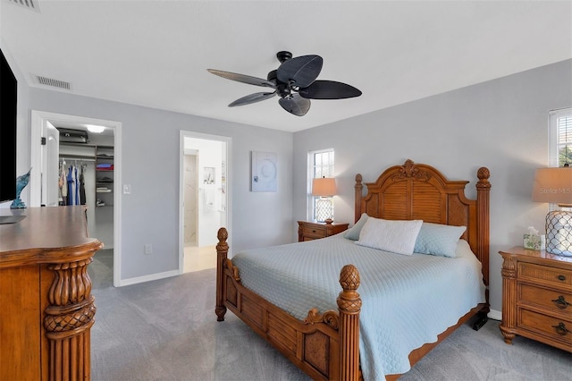 carpeted bedroom featuring a walk in closet, a closet, ensuite bath, and ceiling fan