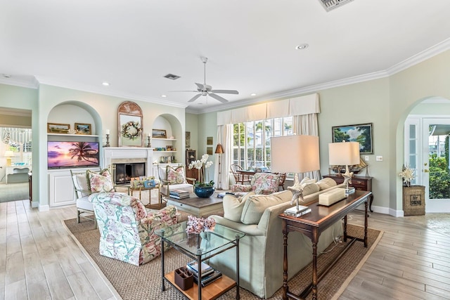 living room with built in features, light hardwood / wood-style flooring, ceiling fan, and ornamental molding