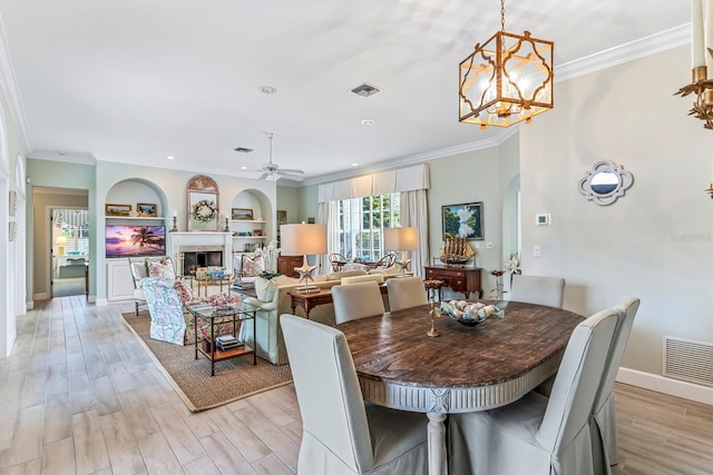 dining area with built in shelves, ornamental molding, ceiling fan with notable chandelier, and light wood-type flooring