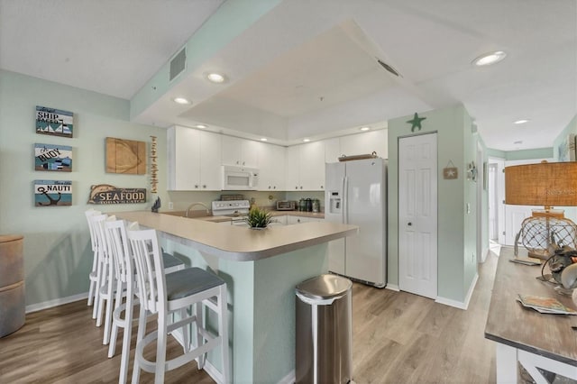 kitchen with a breakfast bar, white appliances, white cabinets, light hardwood / wood-style floors, and kitchen peninsula