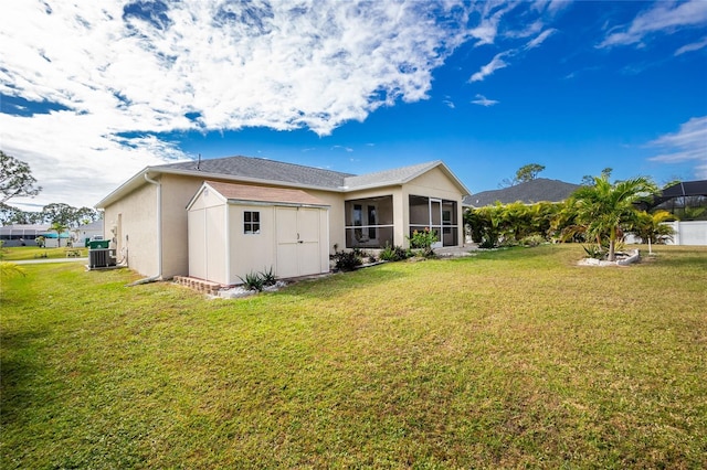 back of property featuring central AC unit, a lawn, a sunroom, and a storage shed