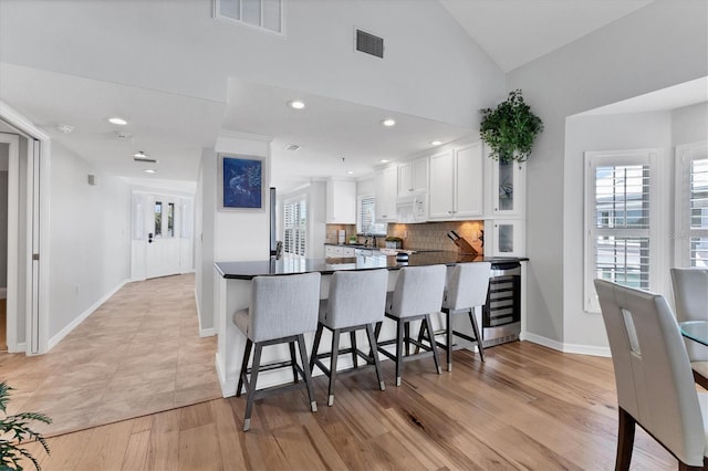 kitchen with white cabinets, decorative backsplash, light hardwood / wood-style floors, kitchen peninsula, and a breakfast bar area