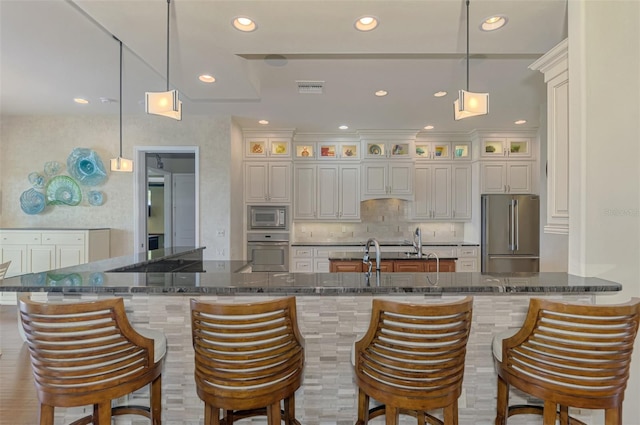 kitchen featuring white cabinets, stainless steel appliances, hanging light fixtures, and dark stone countertops