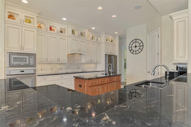 kitchen with oven, built in microwave, dark stone counters, and sink