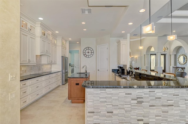 kitchen with a kitchen island with sink, sink, stainless steel fridge, black electric cooktop, and decorative light fixtures