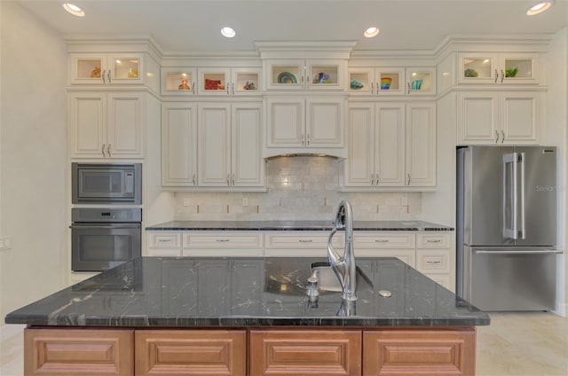 kitchen with decorative backsplash, appliances with stainless steel finishes, a kitchen island with sink, and dark stone countertops