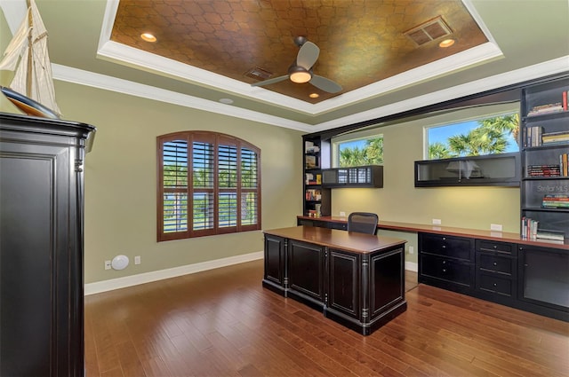 office with a tray ceiling, ceiling fan, crown molding, built in desk, and dark hardwood / wood-style floors