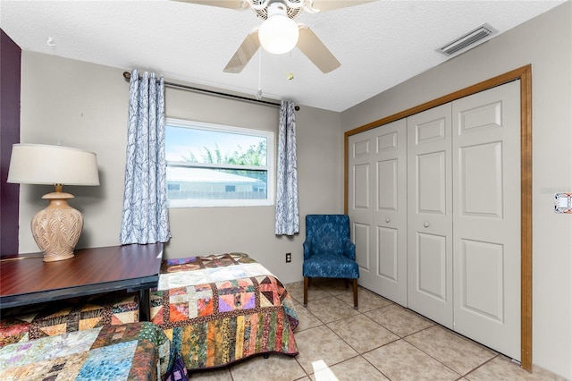 bedroom with a textured ceiling, a closet, ceiling fan, and light tile patterned flooring