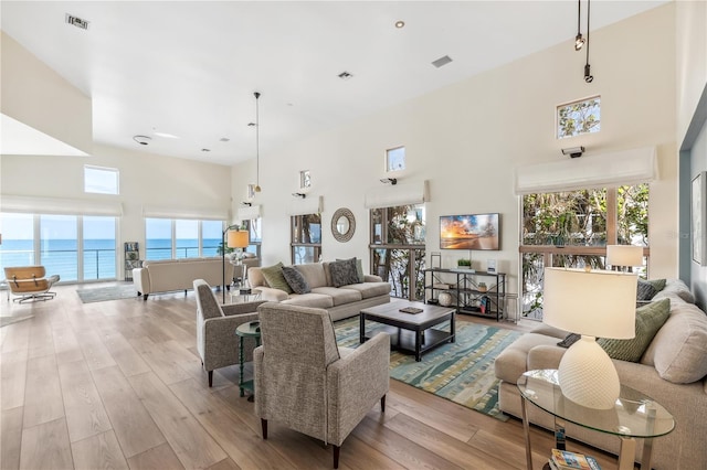 living room featuring a towering ceiling, a water view, and light hardwood / wood-style floors