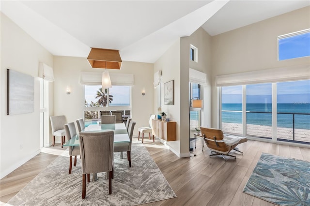 dining room featuring a towering ceiling, a water view, and wood-type flooring