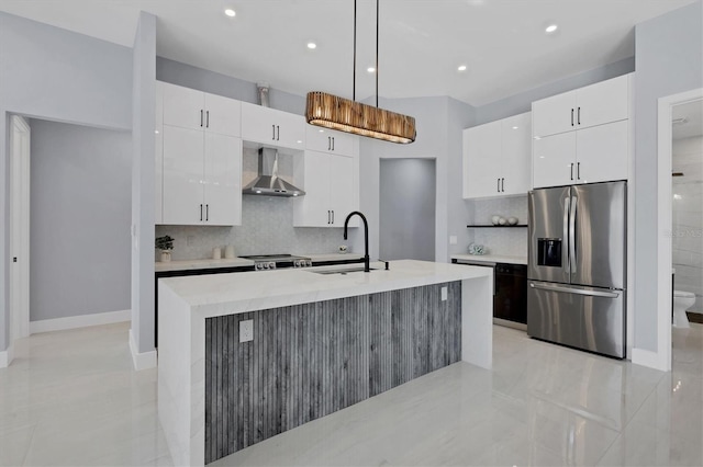 kitchen featuring white cabinets, a center island with sink, wall chimney exhaust hood, appliances with stainless steel finishes, and decorative light fixtures