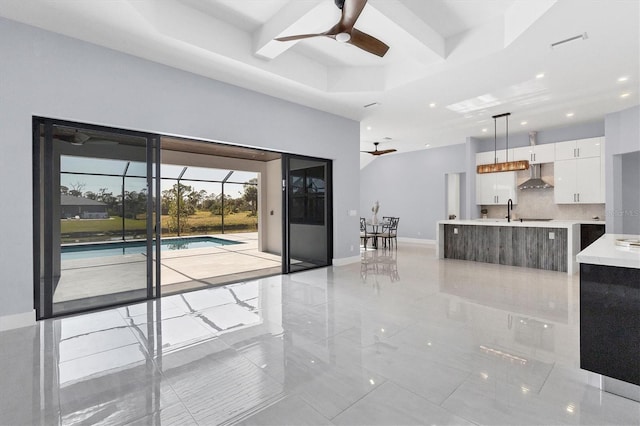 unfurnished living room with a raised ceiling, ceiling fan, and sink