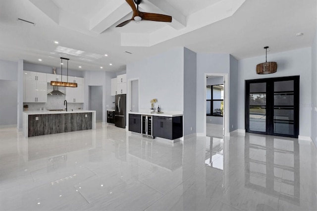 interior space featuring white cabinets, ceiling fan, an island with sink, decorative light fixtures, and stainless steel refrigerator