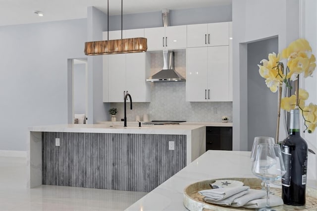 kitchen with decorative backsplash, white cabinetry, hanging light fixtures, and wall chimney exhaust hood