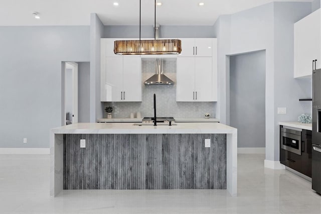 kitchen featuring a center island with sink, white cabinetry, and wall chimney range hood