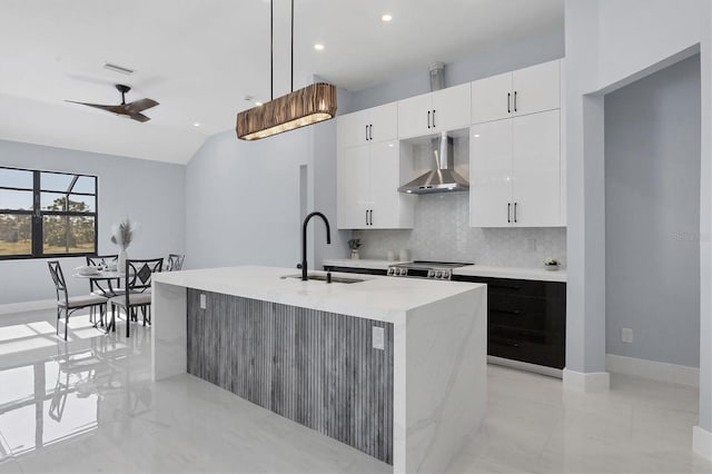 kitchen with white cabinetry, sink, wall chimney exhaust hood, decorative light fixtures, and a center island with sink