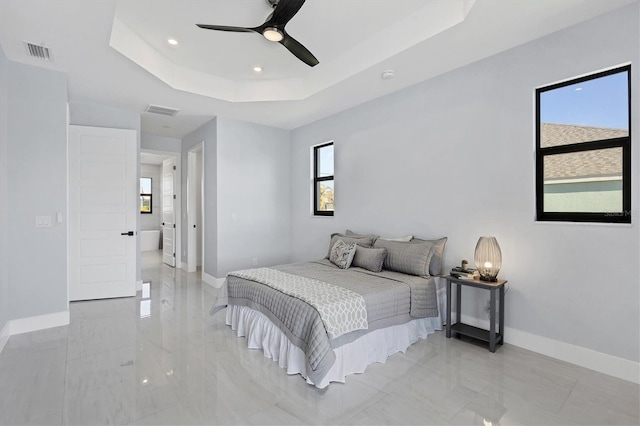 bedroom with a tray ceiling, multiple windows, ceiling fan, and connected bathroom