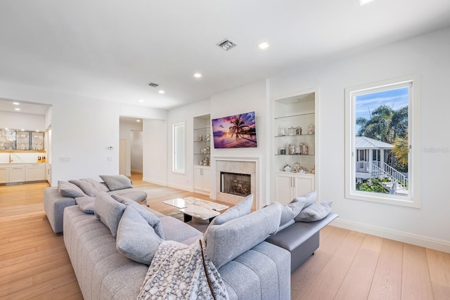 living room with built in features, light wood-type flooring, and a wealth of natural light