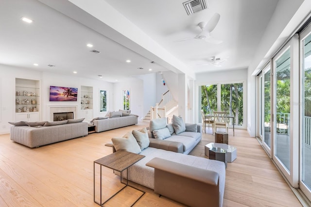 living room with built in shelves, light hardwood / wood-style floors, plenty of natural light, and ceiling fan