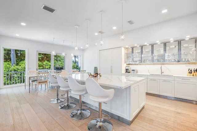 kitchen featuring a center island, sink, hanging light fixtures, light hardwood / wood-style floors, and white cabinetry