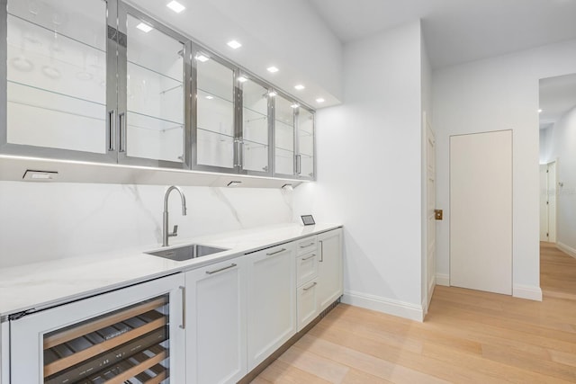 bar with wine cooler, sink, white cabinets, and light hardwood / wood-style flooring