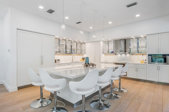 kitchen featuring decorative light fixtures, a kitchen island, wall chimney exhaust hood, and light hardwood / wood-style floors