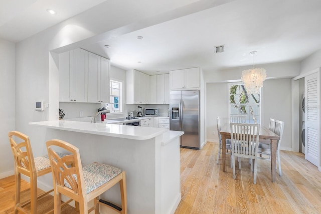 kitchen with pendant lighting, an inviting chandelier, white cabinets, appliances with stainless steel finishes, and light hardwood / wood-style floors